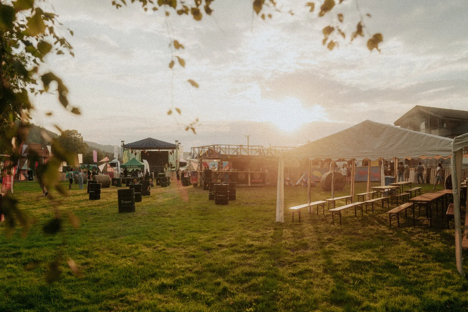 Terenul festivalului Amestec la apus, cu scena în fundal, un cort mare cu mese și bănci de lemn și butoaie așezate pe iarbă