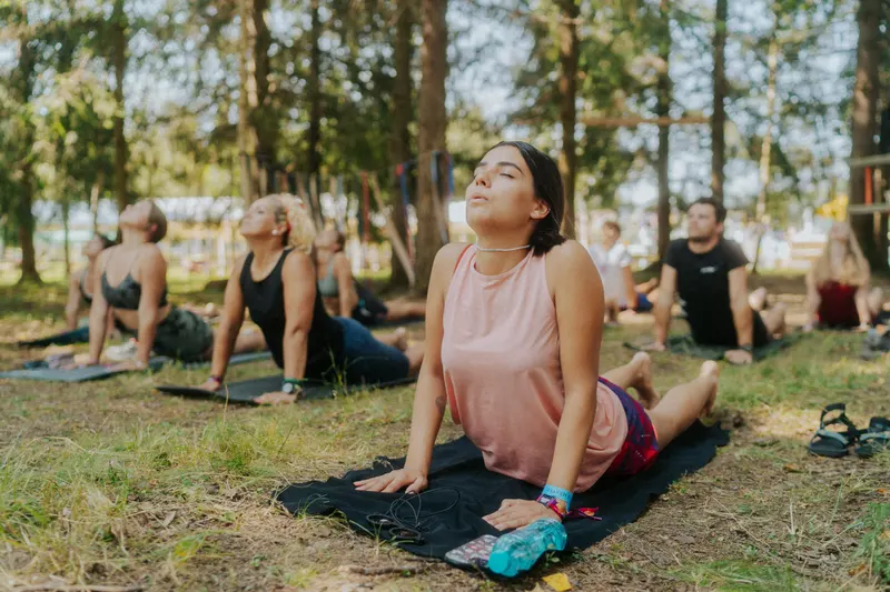 Sesiune de yoga pe saltele întinse pe iarbă, la umbra copacilor, la ediția din 2024
