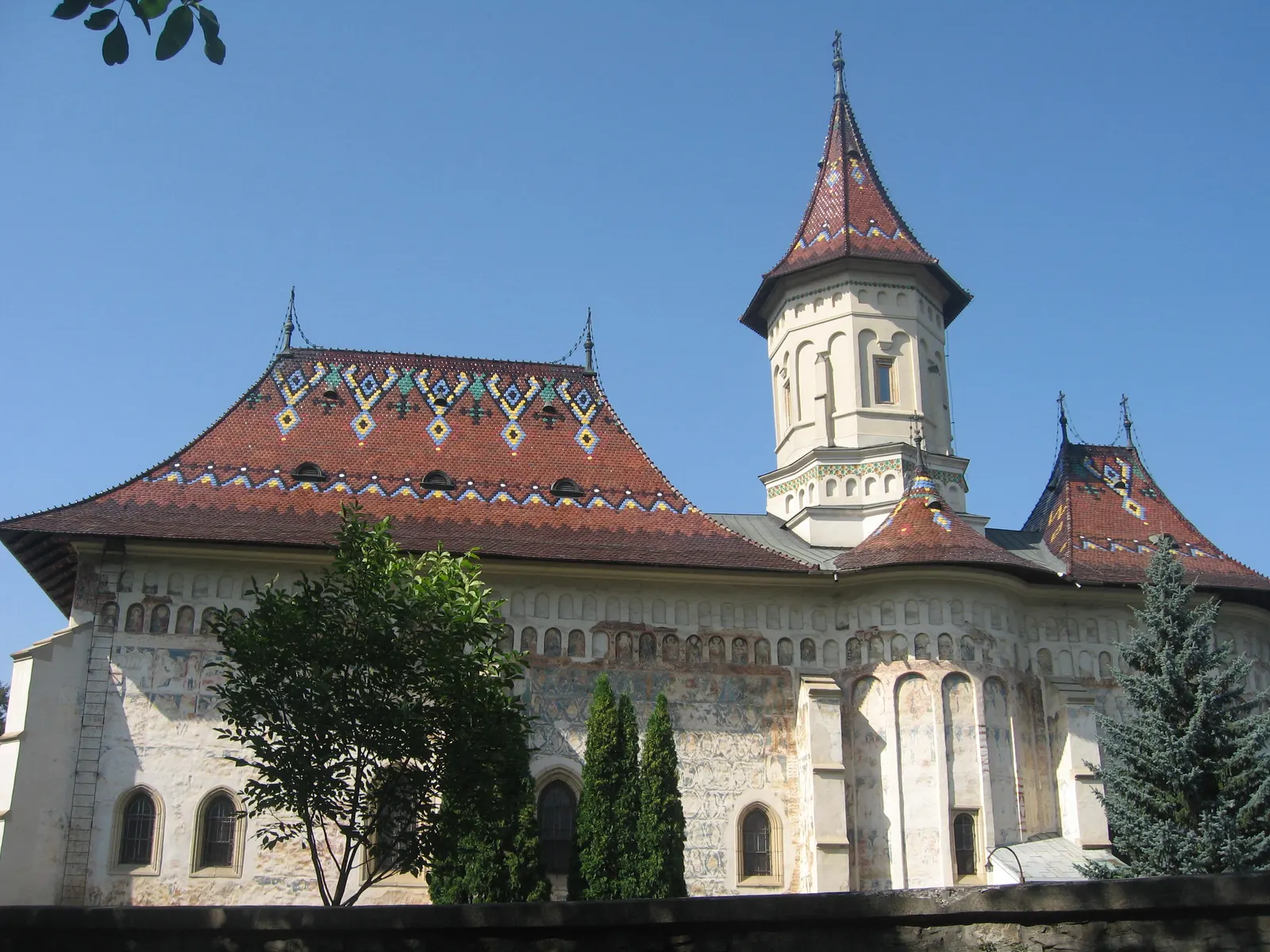 Latura de sud a bisericii Sfântul Gheorghe din Suceava, cu urme decolorate de fresce pe pereți și pe abside, sub acoperișul de țiglă smălțuită cu romburi galbene, albastre și verzi