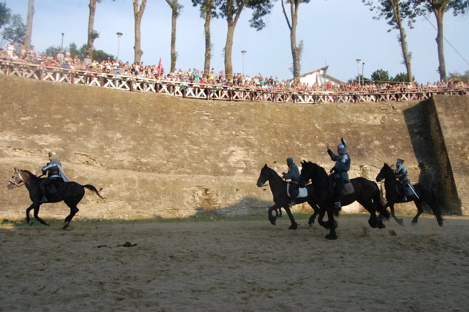 Cavaleri în armură, călare, în șanțul de apărare al Cetății de Scaun, priviți de publicul adunat sus, pe marginea zidului