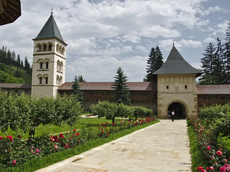 Aleea cu trandafiri din incintă: în stânga, turnul clopotniță cu ferestre în arcade, în dreapta, turnul de poartă numit Turnul Eminescu, legate de zidul cu drum de strajă acoperit