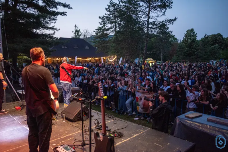 Concert văzut de pe scenă: publicul de la gard și, în spate, clădirea de lemn a Hanului Ariniș, luminată cu ghirlande