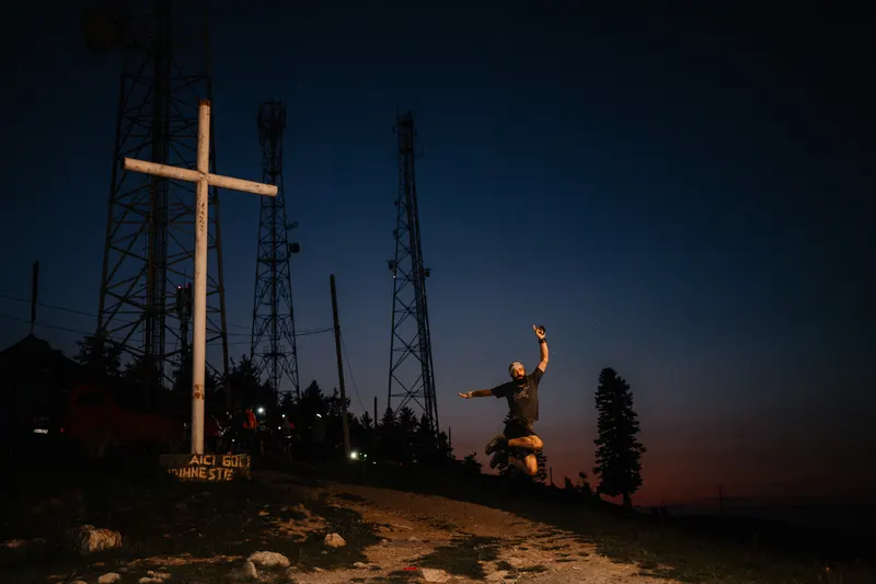 Alergător sărind în aer lângă o cruce albă de pe vârful unui deal, la lăsarea întunericului, în timpul Night Run