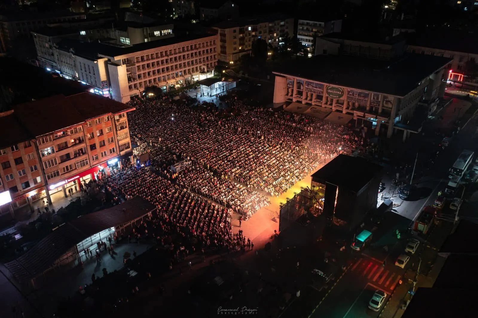 Vedere de sus, noaptea, a Esplanadei Casei de Cultură din Suceava, plină de spectatori așezați pe scaune în fața scenei luminate de la „Simfonii de Toamnă”